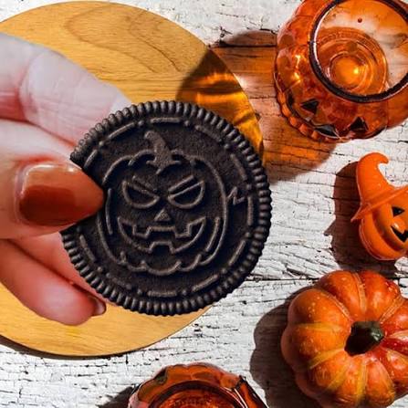 Halloween Oreo cookie held above seasonal treats