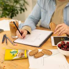 belVita Vanilla Mocha biscuits beside coffee while a person writes in a notebook.